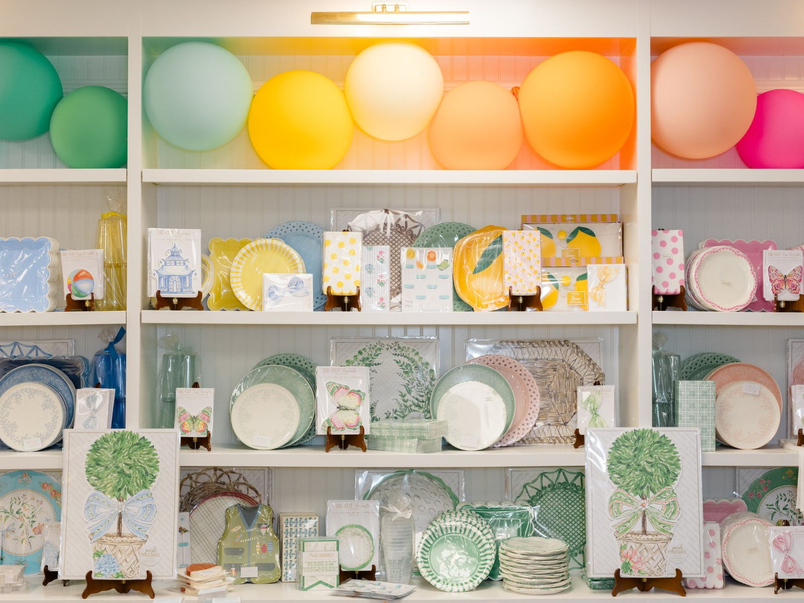 Shelves of party goods beneath a rainbow balloon display in the Party Properly shop