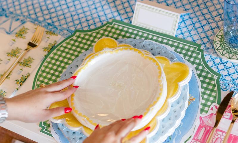 Hands layering scalloped plates over a green gingham placemat